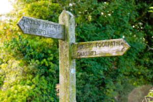 Wooden public footpath signpost pointing to Cartmel and Hampsfell in the Lake District