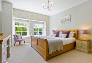 A bright bedroom featuring a king-size bed with colourful cushions, a modern wooden wardrobe, and a large window letting in natural light.