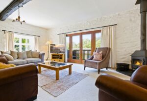 Cosy cottage living room with a log-burning stove, stone fireplace, leather sofas, and exposed stone wall.