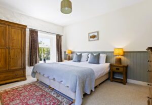 A spacious bedroom featuring a super king-size bed with crisp white linen, a wooden headboard, and matching bedside tables under soft lighting.